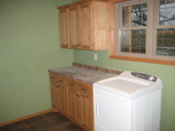 A light green laundry room with tan marble counter tops and wood cabinets